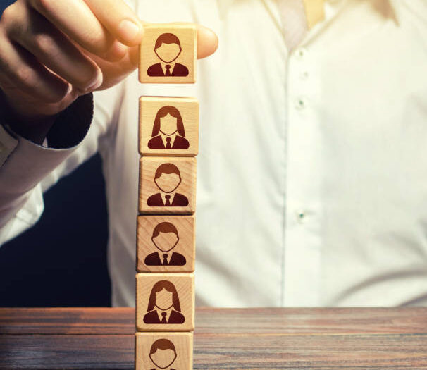 Business leader builds a people block tower. Definition of people in a hierarchical system. Meritocracy. Company organization. Hiring, recruiting workers. Leadership skills, team personnel management.