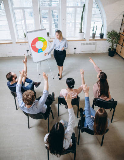 Explaining. Female speaker giving presentation in hall at university workshop. Audience or conference hall. Top view of unrecognized participants. Scientific, business event, training. Education