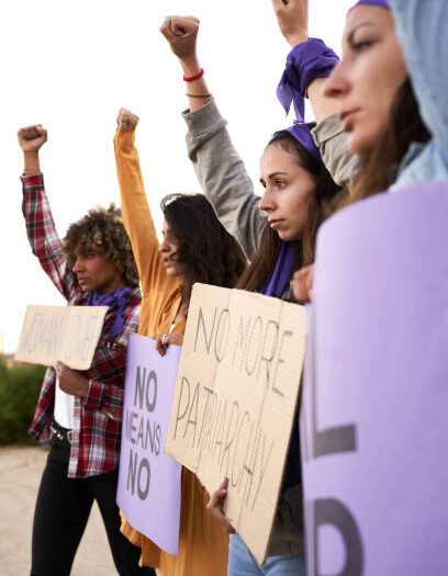 Vertical photo of a group of women marching on the road in protest. Young woman holding a protest sign about women empowerment. Feminist banners.